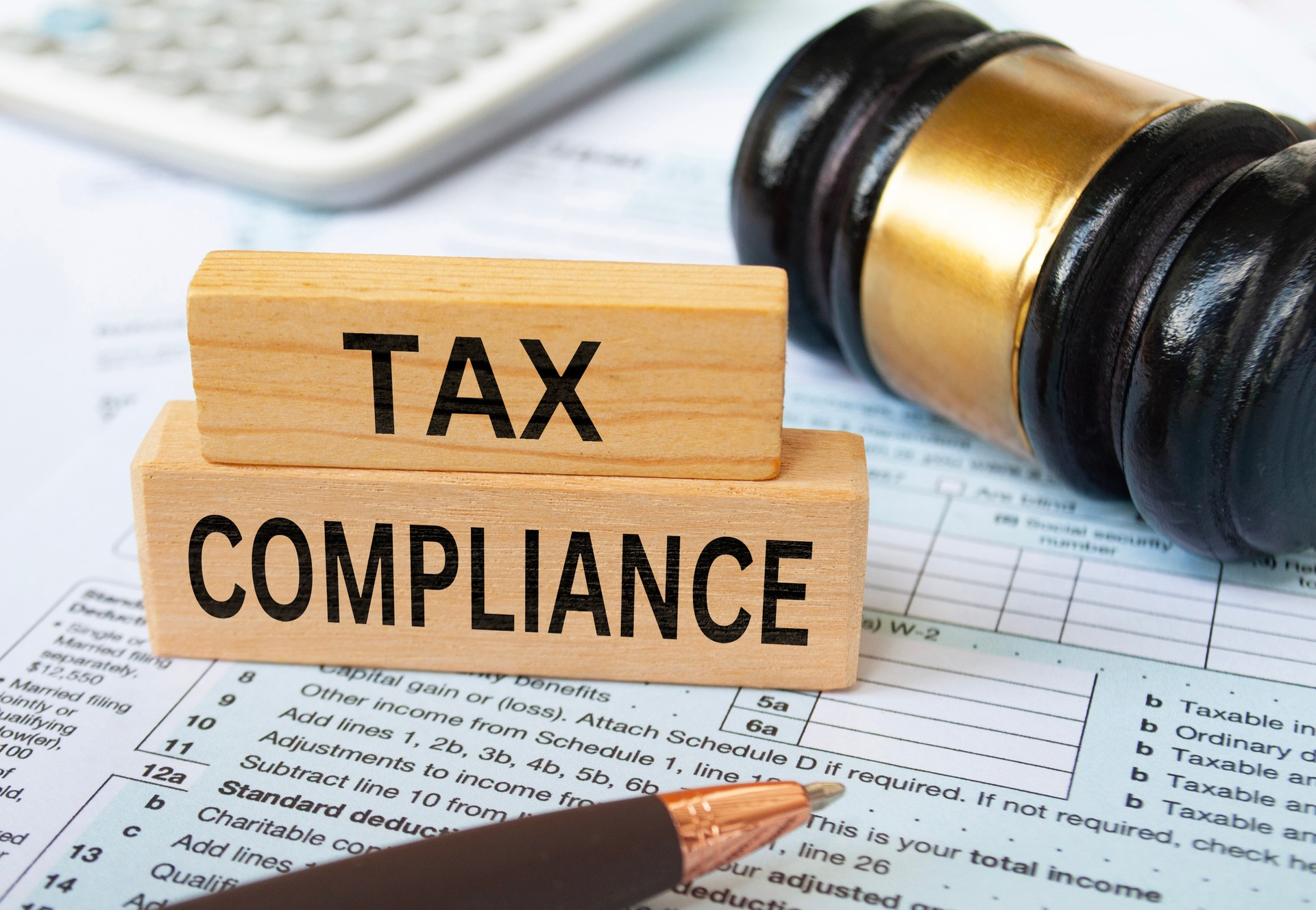 Tax compliance text on wooden blocks with tax form, gavel and calculator background. Taxation concept